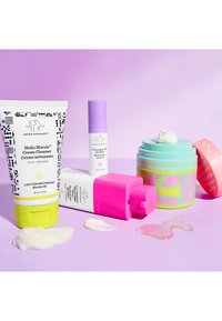 Three cosmetic products on a purple background: a patterned tube, a pastel jar with design elements, and a stick applicator.
