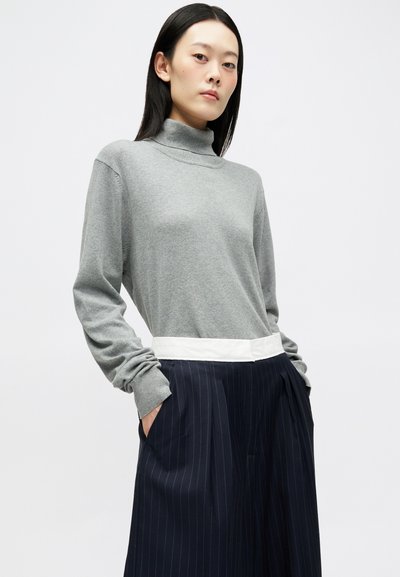 Pelēks garām piedurknēm turtlenecks džemperis ar brīvu piegriezumu, apvienots ar tumši zilu svītrotu augsto jostasvietu biksēm un baltu jostasvietu.