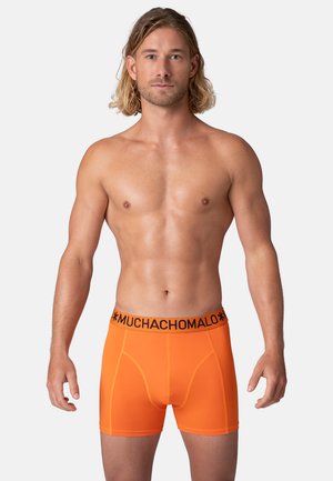 Oranžid bokserid musta "MUCHACHO" vööga, mis pakuvad mõnusat istuvust ja sileda elastse kanga. 