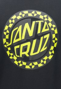 Černé tričko s velkým kulatým logem v jasně žluté barvě, na kterém je text "SANTA CRUZ" a vzor šachovnicového rámečku.