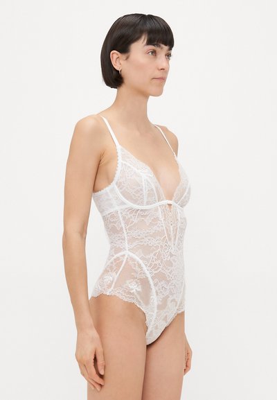 Weißes Spitzen-Bodysuit mit tiefem V-Ausschnitt, dünnen Trägern, floralen Mustern, transparenter Textur und einer taillierten Passform, die aufwendige Details zur Schau stellt.