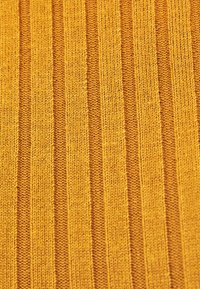 Gros plan sur un tissu tricoté vertical à côtes jaune et moutarde avec des rayures texturées alternant entre étroites et larges.
