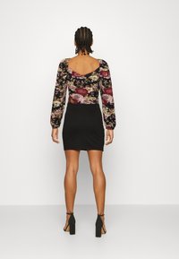 Blusa de manga longa, floral, com um fundo preto e flores roxas e vermelhas, combinada com uma saia preta ajustada. Tecido suave.