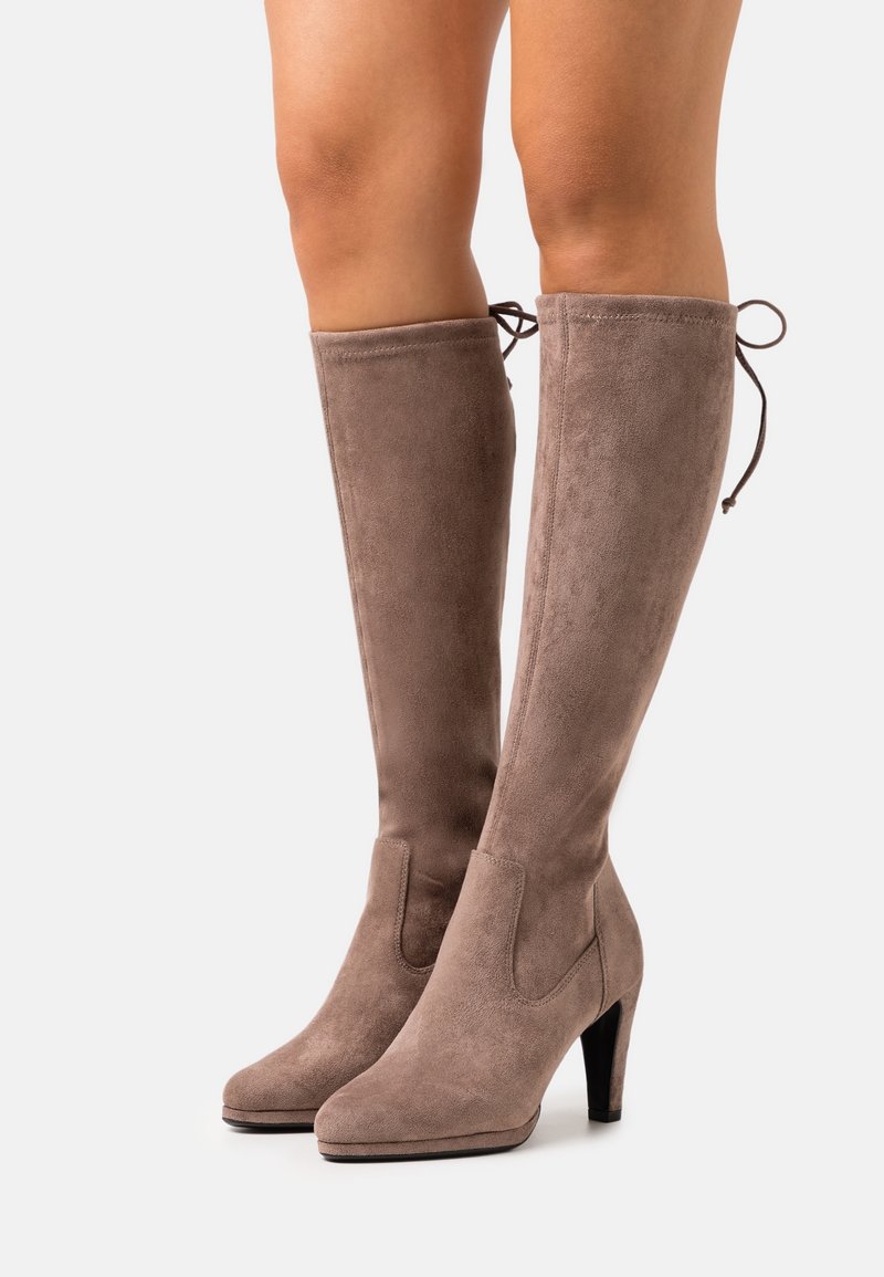 Bottes en daim taupe montant jusqu'au genou, avec un talon bloc et un bout arrondi. Dotées d'un détail de couture et d'un accent noué à l'arrière pour l'ajustement.