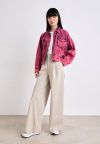 Giacca di jeans rosa, T-shirt bianca, pantaloni beige a gamba larga e scarpe in bianco e nero. Texture liscia, vestibilità rilassata e contrasto di colori distintivo.