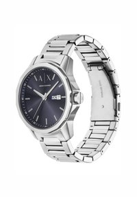 Reloj de acero inoxidable plateado con caja octogonal, esfera azul oscuro, marcadores de hora blancos y un display de fecha; diseño de pulsera de eslabones flexibles.