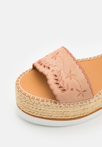 Sandale à plateforme couleur fauve avec semelle en jute tressé et bride en daim rose ornée de broderies florales et de bords festonnés.