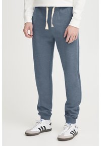 Pantalones de chándal grises con cintura ajustable, diseño de pierna ajustada, textura suave y bolsillos laterales, combinados con zapatillas deportivas blancas y negras.