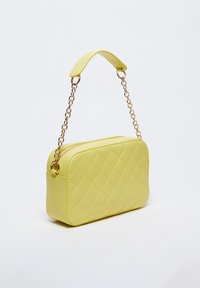 Borsa a tracolla gialla in tessuto trapuntato, dalla forma rettangolare, realizzata in pelle liscia, con tracolla a catena. Presenta una chiusura con zip e dettagli laterali.