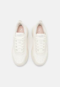 Sneaker bianche con una parte superiore liscia e testurizzata e dettagli perforati, con un accento rosa chiaro sul linguetta. I lacci sono legati in modo uniforme.