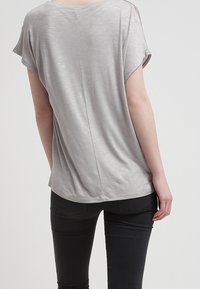 Top gris de manga corta con un corte holgado, que presenta una textura suave y una costura central que recorre la parte posterior. Combinado con jeans negros.