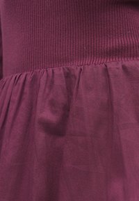 Bordo värvi kleit, millel on soonikkoes bodi ja kogutud, voolav seelik. Kangas on sile ja veidi läikiv.