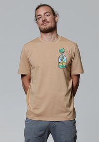 Beige T-shirt met korte mouwen van zachte stof, voorzien van een kleurrafische afbeelding van een palmboom in een fles op de linkerborst.