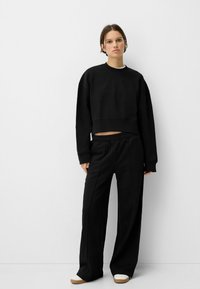 Črna skrajšana hupeerica v kombinaciji s sproščenimi črnimi hlačami. Obe sta izdelani iz mehke tkanine, imata preprost dizajn in elastiko v pasu.