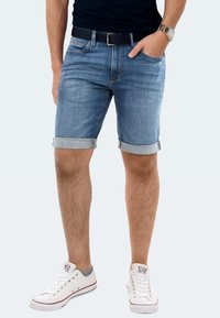Denim shorts in light blue with rolled cuffs, featuring a classic five-pocket design and a dark belt. Paired with white sneakers.
