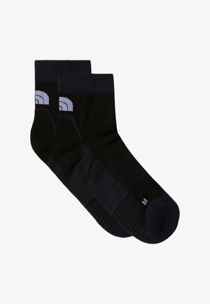 Gilet léger orange par-dessus une chemise à manches courtes blanche, associé à un short bleu clair et des chaussures de sport bleues. Le gilet est doté d'une fermeture éclair noire.