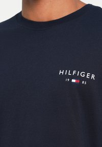 Navy blue cotton T-shirt with a crew neckline, featuring white embroidered "HILFIGER" text and a small logo with red, white, and blue accents.