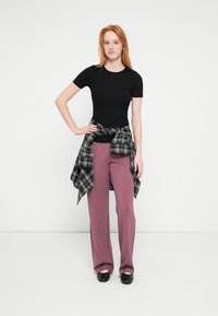 Sort T-shirt med korte ærmer, højtaljede mauve bukser og en ternet flannelsskjorte bundet om livet, brugt sammen med sorte sko.