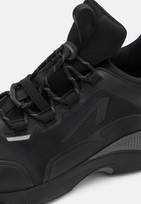 Chaussure de sport noire avec un dessus texturé en maille et matériau synthétique, lacets élastiques et semelle en caoutchouc moulée avec des accents.