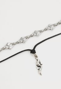 Bracciale in argento con link a forma di stella e collana in corda nera con un charm in argento a forma fluida.