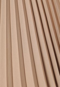 Beige geplooid stof met een gladde textuur, die gelijkmatig verdeelde verticale plooien toont, wat een golfachtig patroon over het oppervlak creëert.