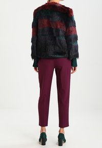 Faux fur jacket with multicolored stripes in burgundy, green, and navy, featuring a loose fit and a soft texture, paired with slim purple pants.