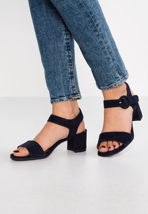 Marineblå ruskindssandaler med blokhæl, der har to brede remme over foden og en ankelrem med en rund spænde.