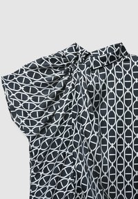 Blusa a maniche lunghe con pattern bianco e nero realizzata in un tessuto leggero e morbido. Presenta un design geometrico con forme circolari e ovali su sfondo nero.