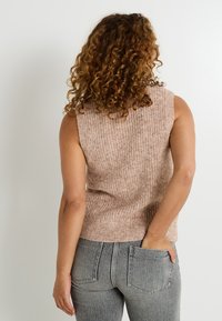 Un top tricoté sans manches rose clair avec une texture côtelée, associé à un jean gris. L'arrière du top est uni, ajusté à la taille.