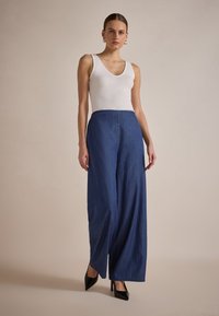 Top sin mangas blanco con canalé combinado con pantalones oscuros de mezclilla de pierna ancha y tiro alto, y tacones de aguja negros. Tejido suave con un ajuste relajado.