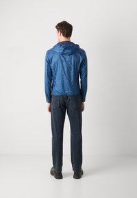 Blaue leichte Jacke mit Kapuze, glatte Textur, Kordelzug am Hals, getragen über dunkelblauen Jeans, von hinten sichtbar.