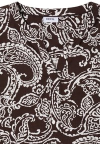 Chemise marron et blanche à motif paisley avec un col en V et une patte de boutonnage avant visible, étiquetée "CECIL" à l'intérieur du col.