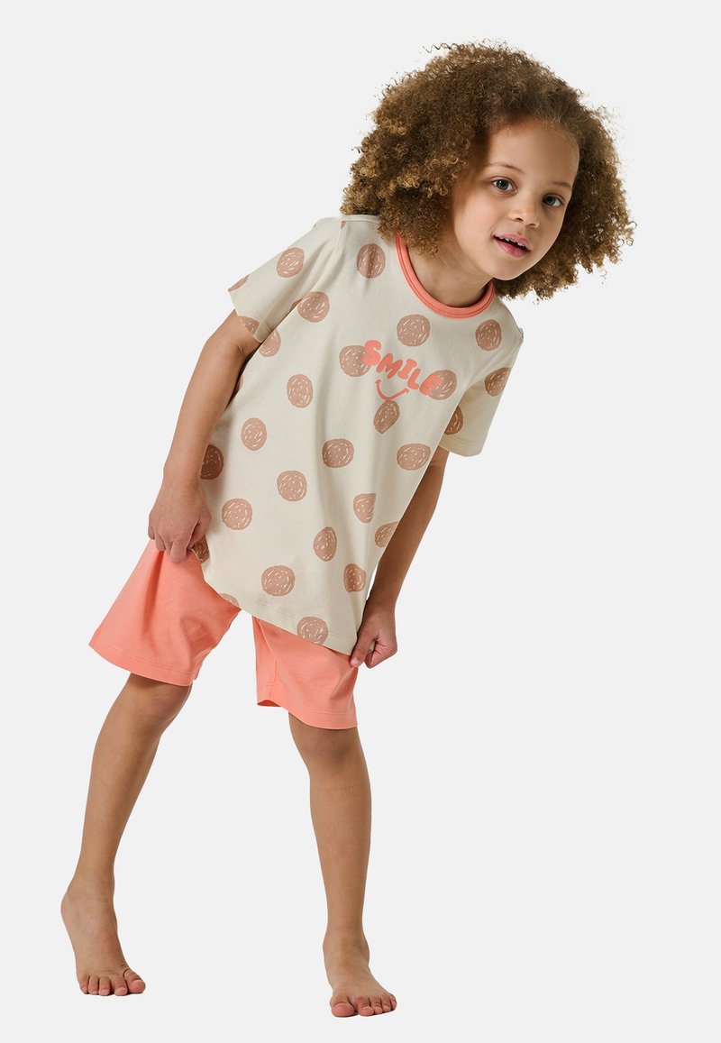 Ljust beige bomullströja med bruna prickar och texten "LE" som är ihop med korallfärgade shorts. Visad på ett barn med lockigt hår.