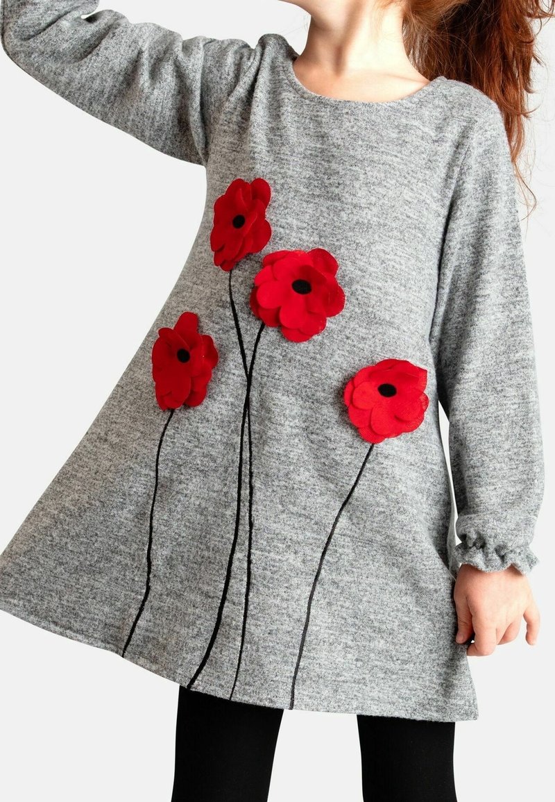 Enfant portant une robe grise à manches longues avec quatre grandes fleurs rouges aux centres noirs et aux tiges noires à l'avant.