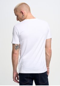 Bílý tričko s krátkým rukávem vyrobené z bavlny. Má klasický kulatý výstřih a jednoduchý design. Žádné vzory ani grafika nejsou viditelné.