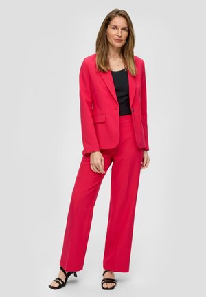 Blazer rose ajusté avec un pantalon large assorti, fabriqué dans un tissu lisse et doté d'un col cranté classique. Porté sur un haut noir et associé à des talons noirs.