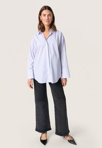 Light blue and white striped oversized button-up shirt with long sleeves, paired with black wide-leg jeans and pointed black flats.
