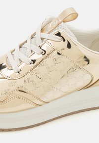 Sneakers metalice aurii cu accente din plasă țesută și șireturi albe. Designul include branding reliefat și o talpă texturată.