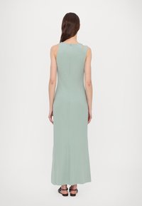 Robe longue, vert menthe, sans manches, fabriquée en tissu lisse. Présente une fermeture éclair et un détail découpé sur l'épaule.