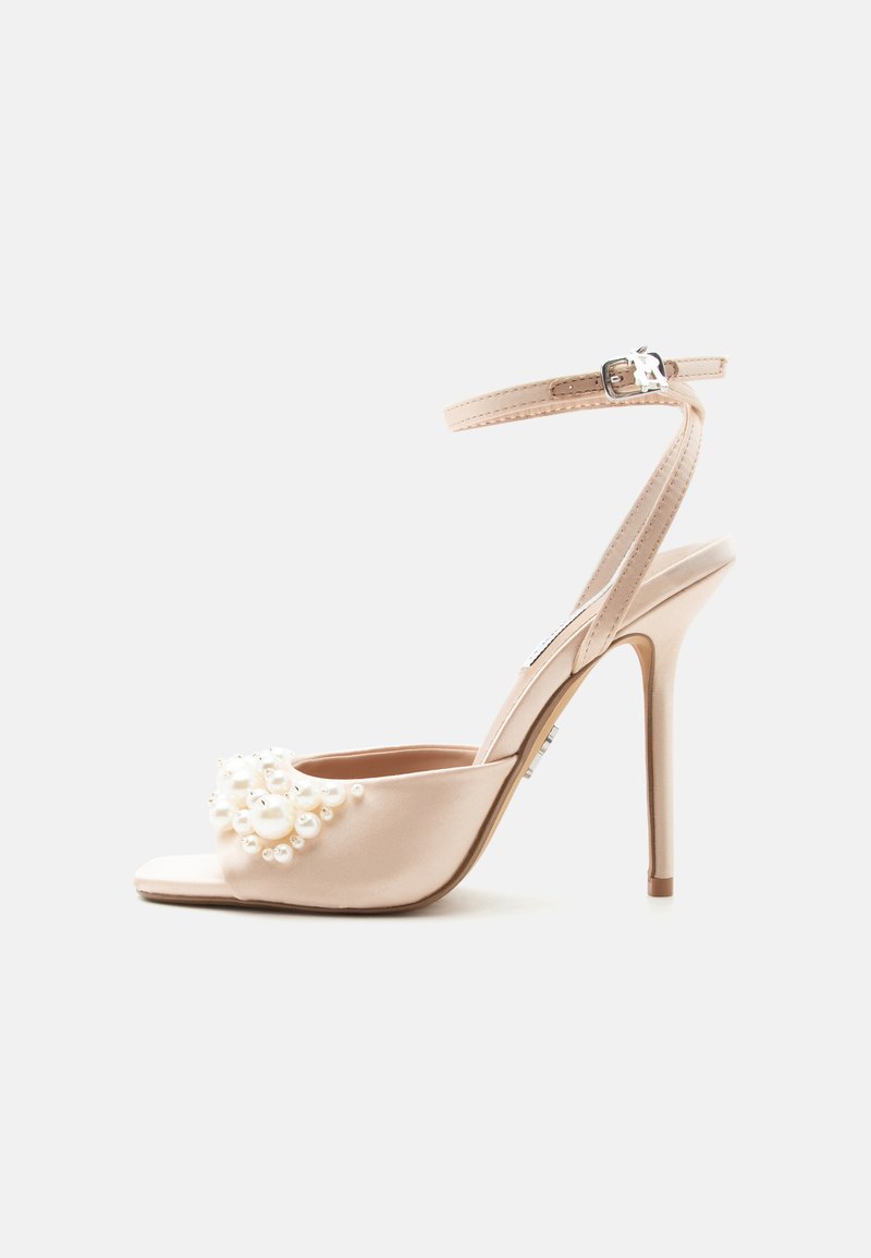 Μπεζ πέδιλο με ψηλό τακούνι και λουράκι στον αστράγαλο με διακοσμήσεις από πέρλες στο μπροστινό λουράκι, εμφανίζεται σε λευκό φόντο.