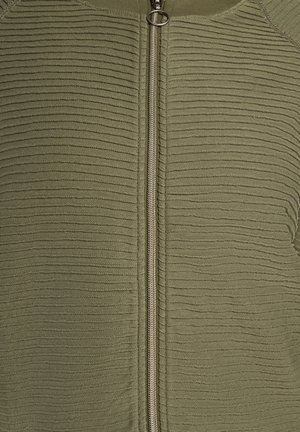 Veste zippée vert olive avec une texture côtelée, dotée d'une fermeture éclair métallique centrale et d'un col arrondi.
