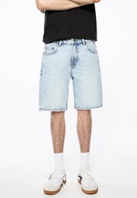 Vaaleansiniset farkkushortsit, polvenmittaiset, rentoa mitoitusta. Ominaisuuksiin kuuluvat etutaskut, ommeltu reuna ja nappikiinnitys.