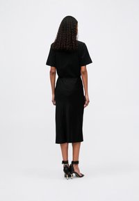 Vestido preto midi com um corte descontraído e mangas curtas, complementado por sapatos de salto com tira no tornozelo. Tecido suave, design minimalista e silhueta elegante.