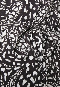 Tecido preto com um padrão abstrato branco, apresentando um detalhe de laço na cintura e uma textura suave. Close-up do design da peça.