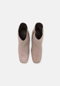 Semišové kotníkové boty v světle taupe barvě s hladkým povrchem, vybavené bočním zipem a zaoblenou špičkou. Ploché podrážky pro stabilitu.