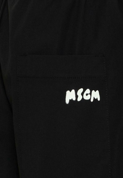 Tissu noir avec une poche carrée cousue dessus, affichant le texte "MSGM" en blanc dans une police audacieuse et irrégulière sur la poche.