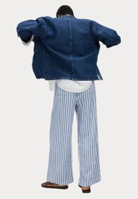 Denimjakke i mørkeblå, oversized pasform, med klassisk krave. Sammen med bredbenede stribede bukser i blå og hvid.