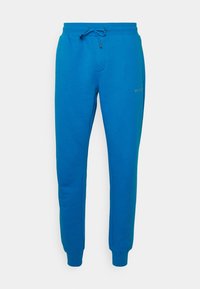 Blue cotton sweatpants with an elastic waistband, drawstring detail, and tapered cuffs; features a subtle logo on the left thigh.