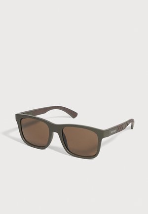 Lunettes de soleil Burberry vert olive, avec des verres rectangulaires bruns et des branches à motifs, sur un fond clair.