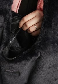 Hand with silver ring unzipping a black inner pocket of a dark gray fuzzy Puma jacket with a pink zipper lining.